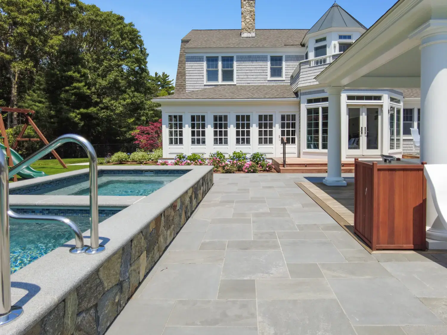 Large format Everblue porcelain pavers laid around a pool at a shingle-style home